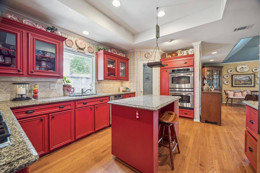 This beautifully appointed granite-clad kitchen is the heart of the home. Glass-front cabinets provide a stylish display for dishware and add an elegant touch to the ample storage. The tray ceiling adds depth and character, enhancing the overall charm of the space. Open to the expansive breakfast room, this kitchen creates a natural hub for everyday living, entertaining, and gathering with family and friends.
