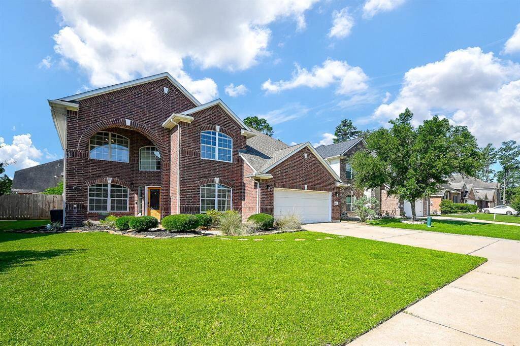 This photo showcases a spacious two-story brick home with a well-maintained lawn, a two-car garage, and a welcoming front entrance. The house features large windows and is situated in a suburban neighborhood with tree-lined streets.