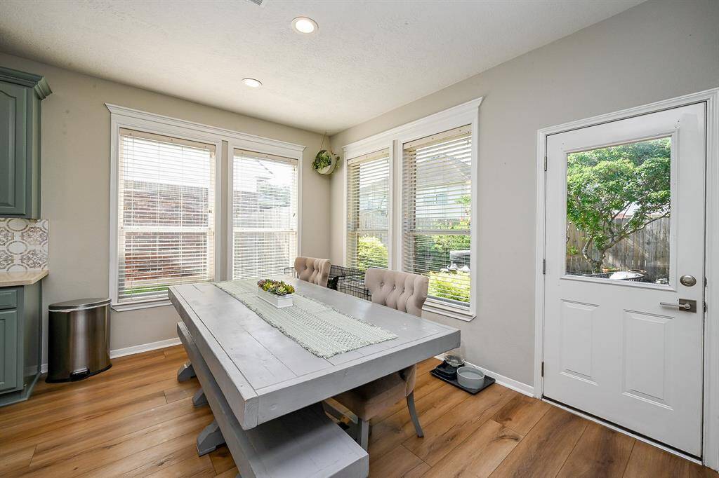 Bright dining area with large windows, room for a large table, and access to a lush backyard. Features vinyl wood look floors, and a welcoming atmosphere.