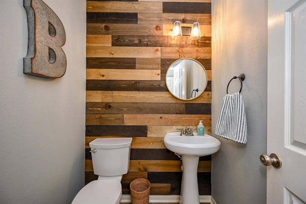This is a stylish half-bathroom featuring a rustic wood accent wall, a round mirror, and modern light fixtures.