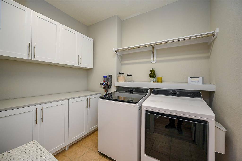 This photo shows a modern laundry room with sleek white cabinets, a spacious countertop, and a shelf for storage. The neutral color scheme adds a clean and organized feel.