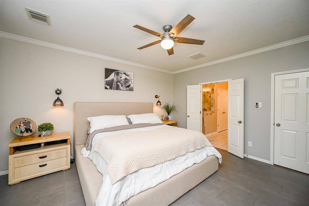 This spacious bedroom features space for a large bed with neutral tones, modern ceiling fan, and ample natural light. It has an en-suite bathroom accessible through double doors. The room exudes a cozy and inviting atmosphere.