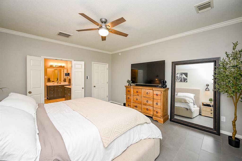 This bedroom features a cozy, neutral color palette with a ceiling fan and tiled flooring.  The room connects to a bright ensuite bathroom with double doors, adding convenience and style.