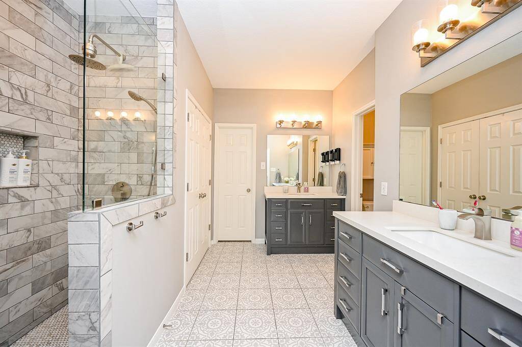 This spacious bathroom features a modern design with a large glass-enclosed shower, dual sinks with dark cabinetry, and stylish tile flooring. Ample lighting and neutral tones create a bright, inviting atmosphere.