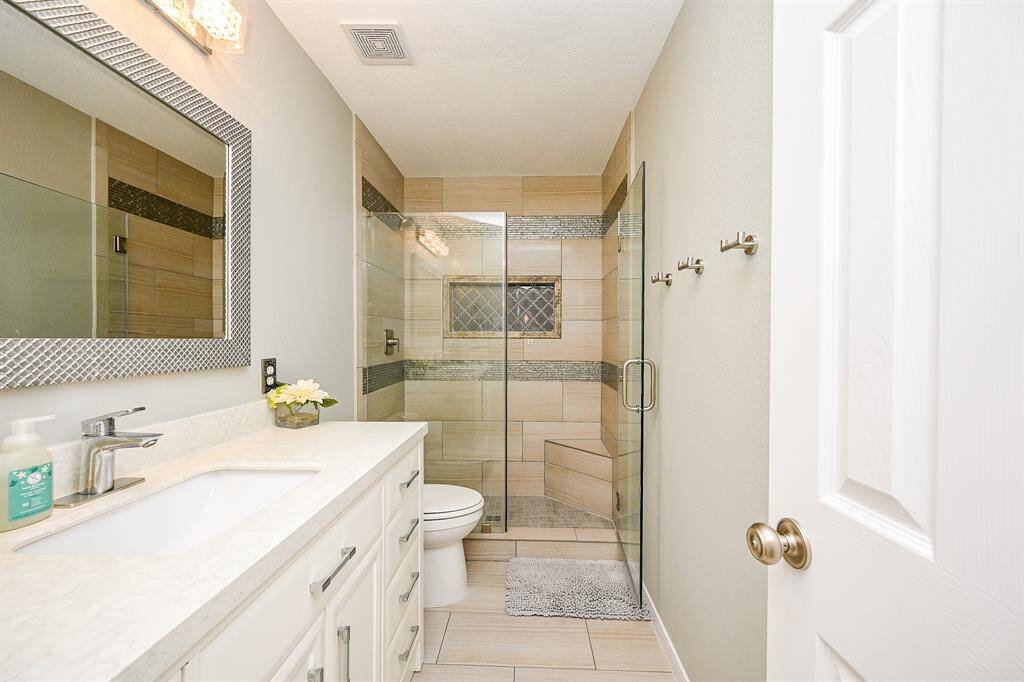 This bathroom features a modern design with a glass-enclosed shower accented by stylish tile work. It includes a sleek vanity with a large mirror, subtle lighting, and neutral tones, creating a clean and inviting space.