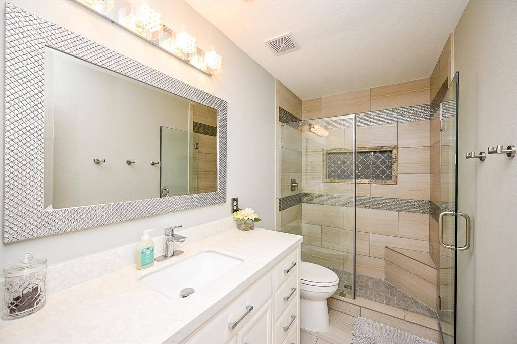 This bathroom features a modern design with a sleek glass-enclosed shower, stylish tile work, and a large vanity with ample storage. The elegant mirror and bright lighting create a fresh and inviting atmosphere.