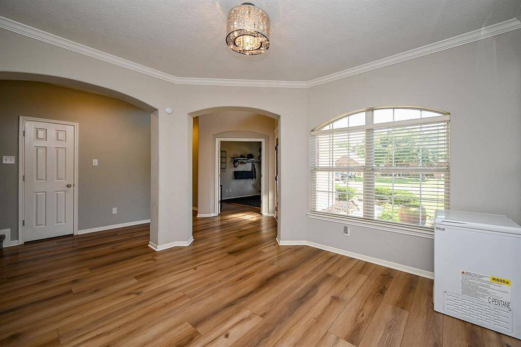 Bright and inviting room with large windows, arched doorways, and wide planked vinyl flooring. Features a modern light fixture and neutral walls, creating a spacious feel. Perfect for a cozy living area or formal dining room.
