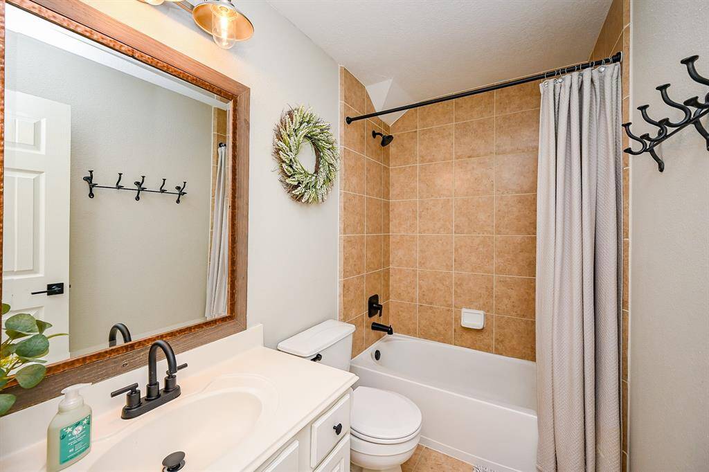 This bathroom features a modern design with a beige tiled bathtub and shower, white vanity with black fixtures, and a large framed mirror.