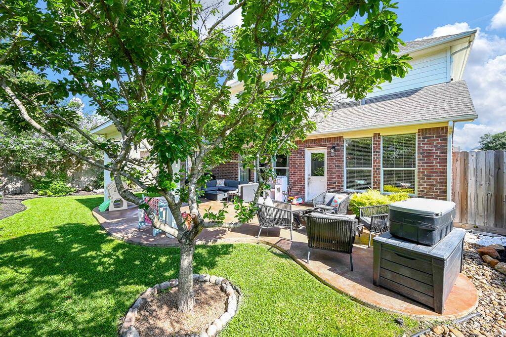 Charming backyard featuring a well-maintained patio area, surrounded by lush green grass and a mature tree. The brick exterior of the house adds character, and there's space for entertaining or relaxing.