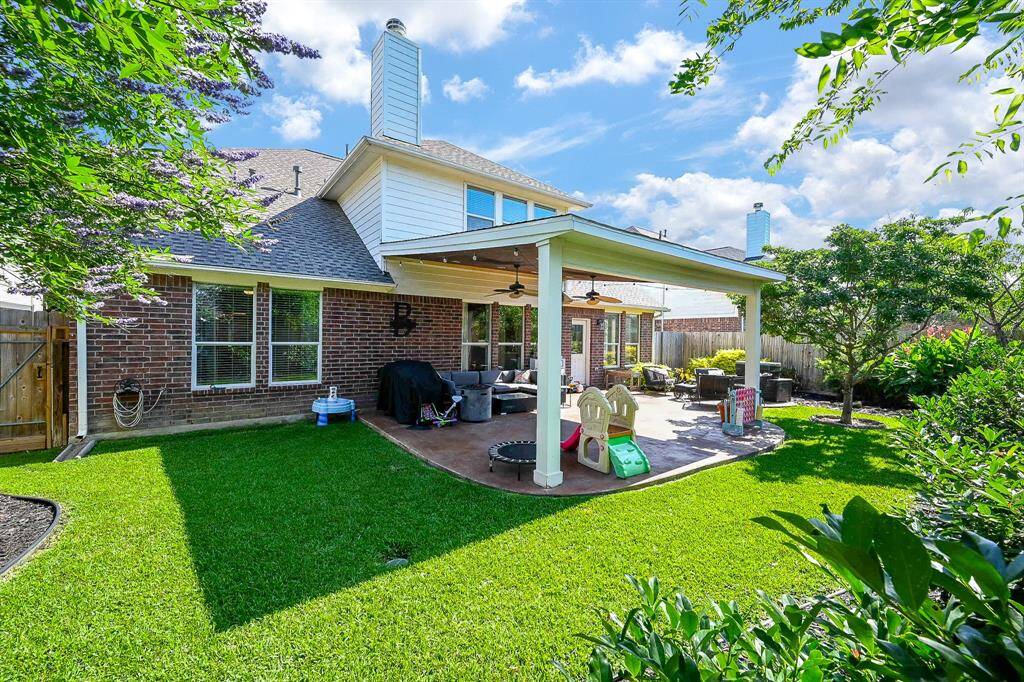 This photo showcases a spacious backyard featuring a well-maintained lawn and a large covered patio area. The patio has a ceiling fan, perfect for outdoor relaxation and entertaining. Mature trees and landscaping add privacy and charm to the space.