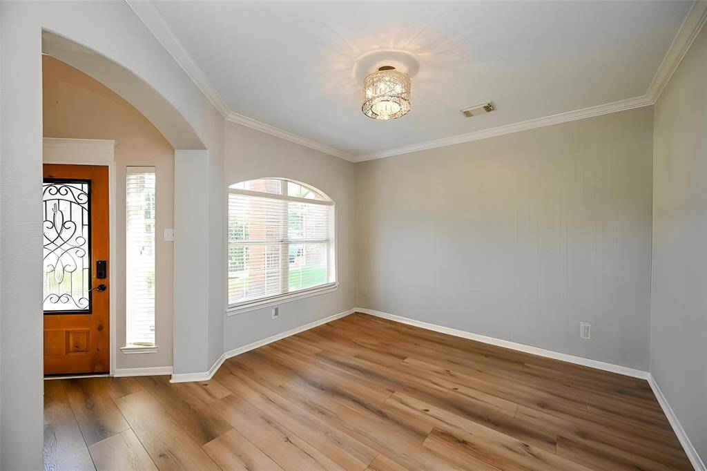 Bright and inviting room with large windows, arched doorways, and wide planked vinyl flooring. Features a modern light fixture and neutral walls, creating a spacious feel. Perfect for a cozy living area or formal dining room.