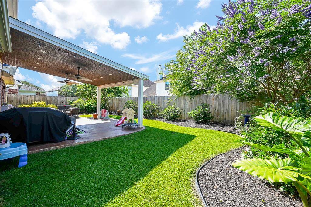 Spacious backyard with a covered patio, ceiling fans, and a well-maintained lawn. Ideal for outdoor relaxation and entertaining, featuring lush landscaping and privacy fencing.
