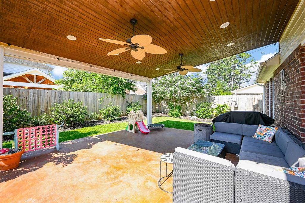 This outdoor space features a covered patio with ceiling fans, and a grill, perfect for entertaining. The fenced yard includes a play area and lush greenery for added privacy and relaxation.