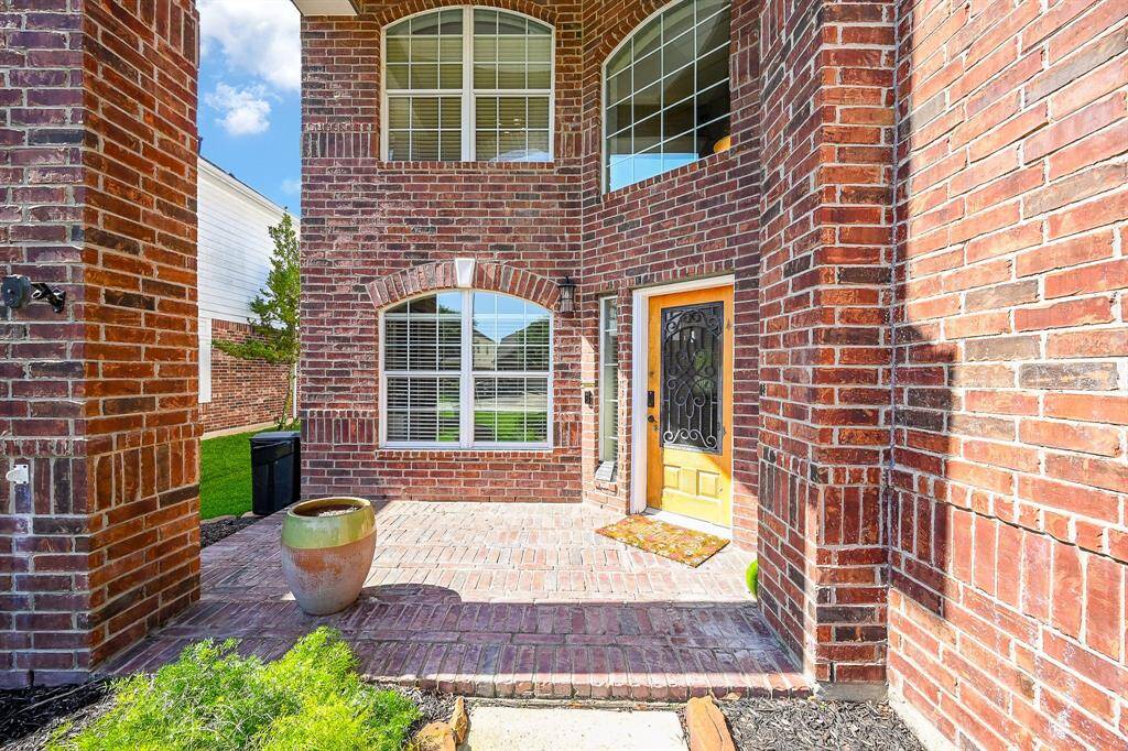 This photo showcases a charming brick exterior entryway with a welcoming wood door, decorative wrought iron accents, and large windows. The space is bright and inviting, featuring a small porch area with a planter, perfect for adding personal touches.