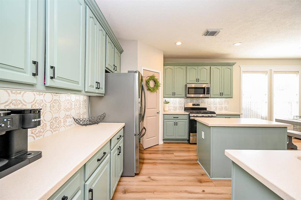 This kitchen features soft green cabinetry, modern stainless steel appliances, and a stylish tile backsplash. Ample counter space and natural light create an inviting and functional cooking area.