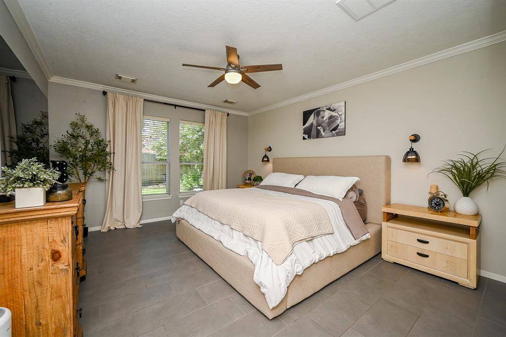 This cozy bedroom features room for a large bed with modern wall sconces, and ample natural light from a set of windows framed by light curtains. The room is complemented by a view of the backyard.