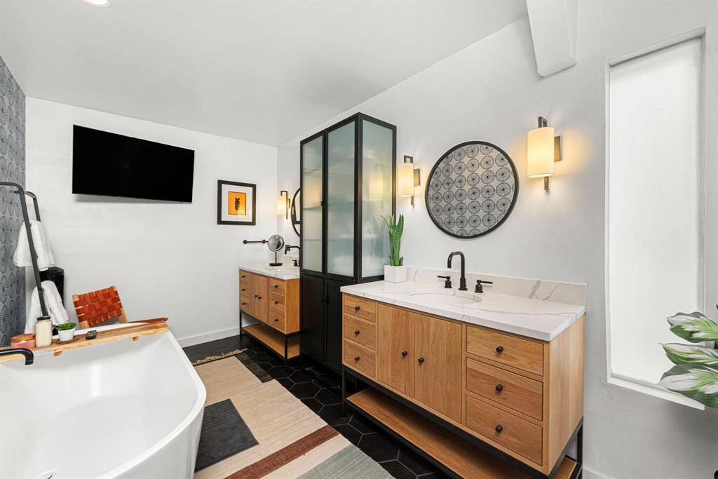 Primary bath has stand-alone tub, dual sinks, black tile flooring.