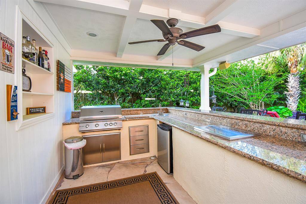 Outdoor kitchen has built in grill, fridge, sink, and cooler.