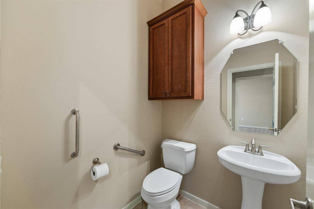 At the left of entryway  there is a convenient half bath. The half bath features tile floors, a pedestal sink, and built-in wooden cabinets for storage.