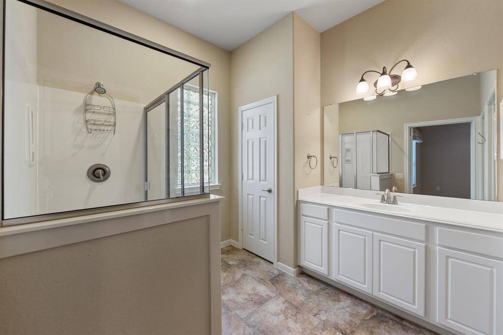 The bathroom includes tile floors, a single vanity with white cabinets and sink, a step-in shower. The bathroom has been conceived as a cozy relaxation retreat.