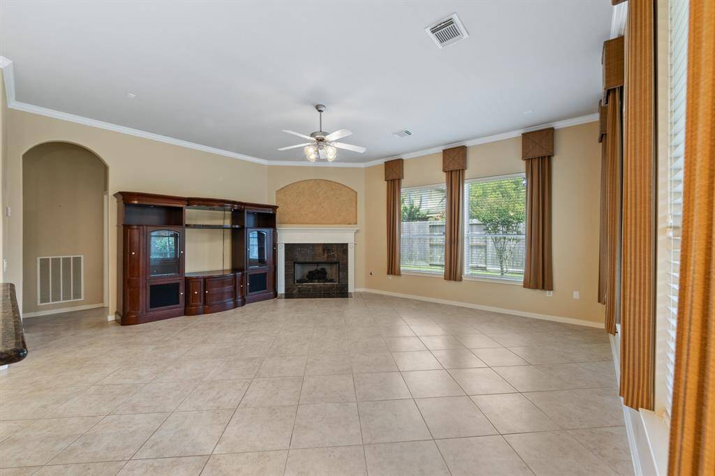 The living room showcases tile floors, crown molding, a cozy gas fireplace, and abundant windows that fill the space with natural light, ceiling fan for an inviting and comfortable atmosphere.
