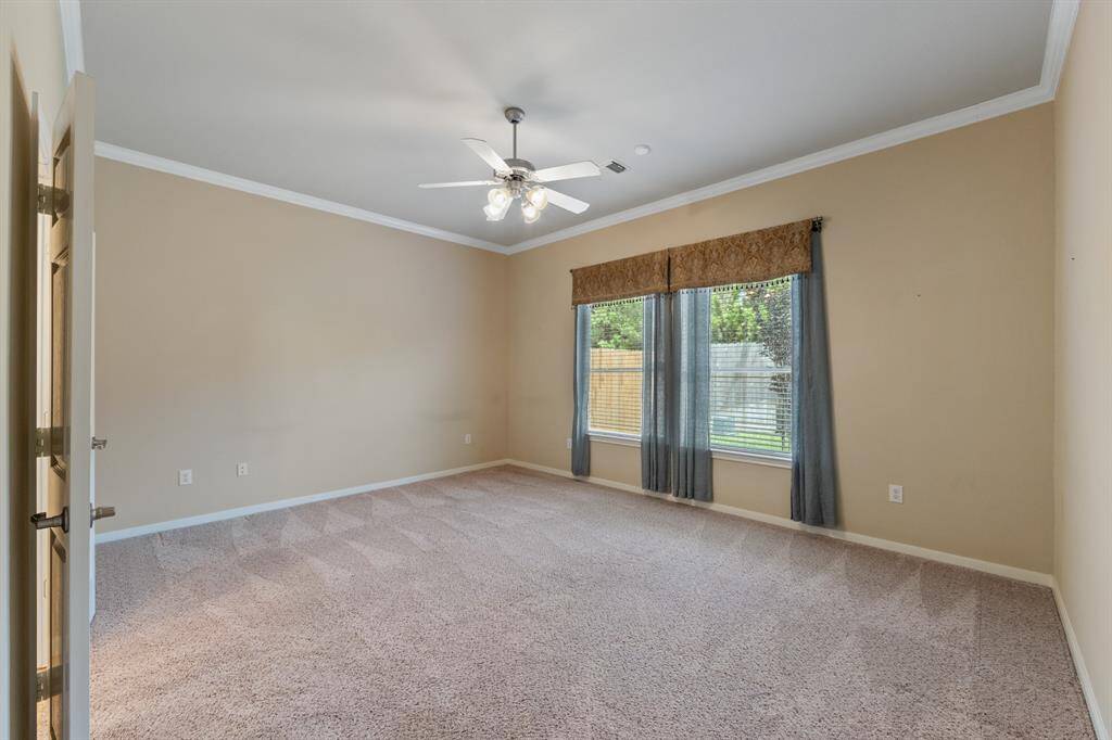 The primary bedroom features soft carpet flooring and elegant crown molding, offering a comfortable and stylish retreat within the home, along with a ceiling fan for ultimate comfort.
