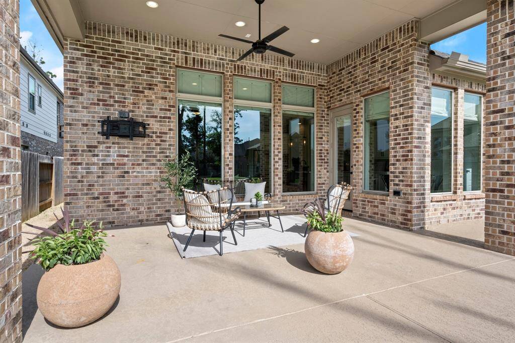 Discover a charming covered patio with brick walls, large windows, and a ceiling fan. It's perfect for relaxing or entertaining, featuring cozy seating and lush potted plants.