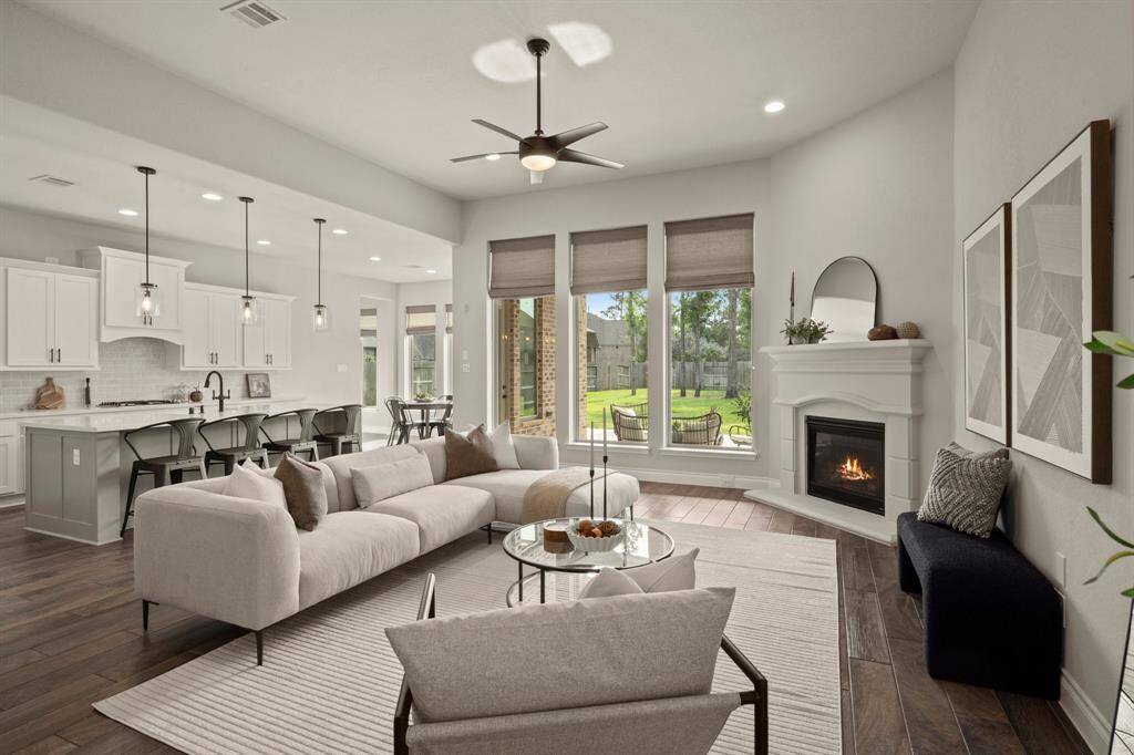 This photo showcases an inviting open-concept living area featuring a modern kitchen with a large island, elegant pendant lighting, and a cozy sitting area with a fireplace. Large windows offer plenty of natural light and a view of the backyard.