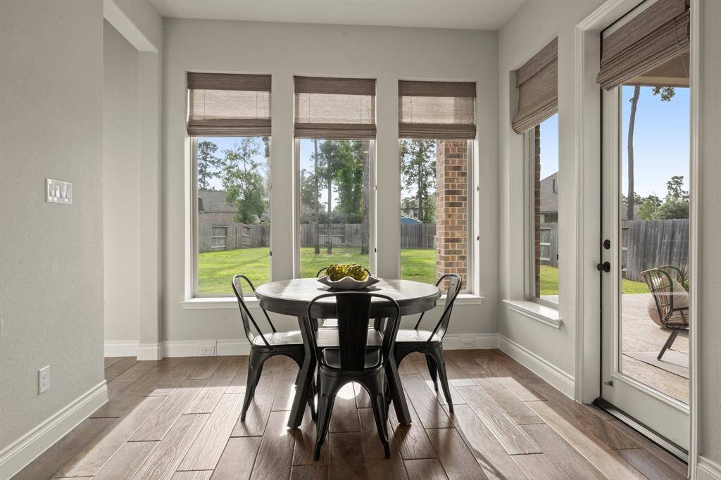 Bright breakfast nook with large windows overlooking the backyard, featuring wood-look tile flooring and patio access through a glass door.