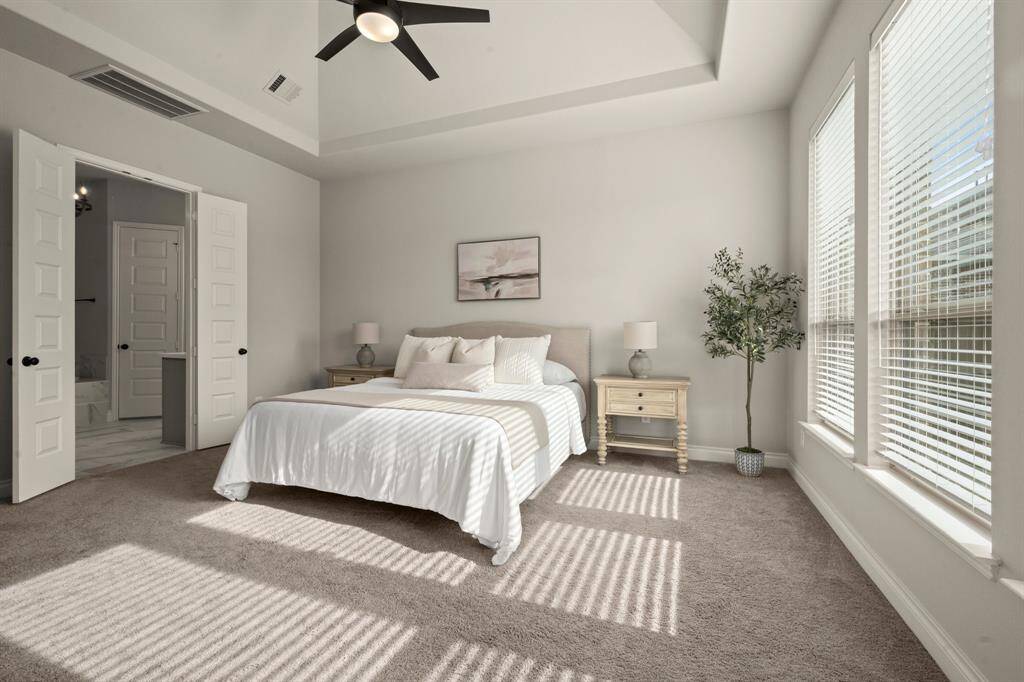 Bright and spacious bedroom with neutral decor, featuring large windows, plush carpeting, and a modern ceiling fan. It includes an ensuite bathroom accessible through double doors, creating a serene and comfortable retreat.