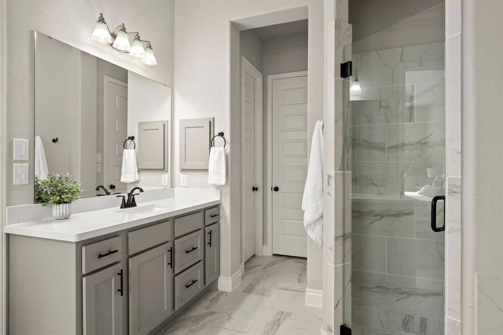 This bathroom features a modern design with a spacious vanity, dual sinks, and sleek fixtures. It includes a glass-enclosed shower with elegant marble tile, offering a clean and sophisticated look.