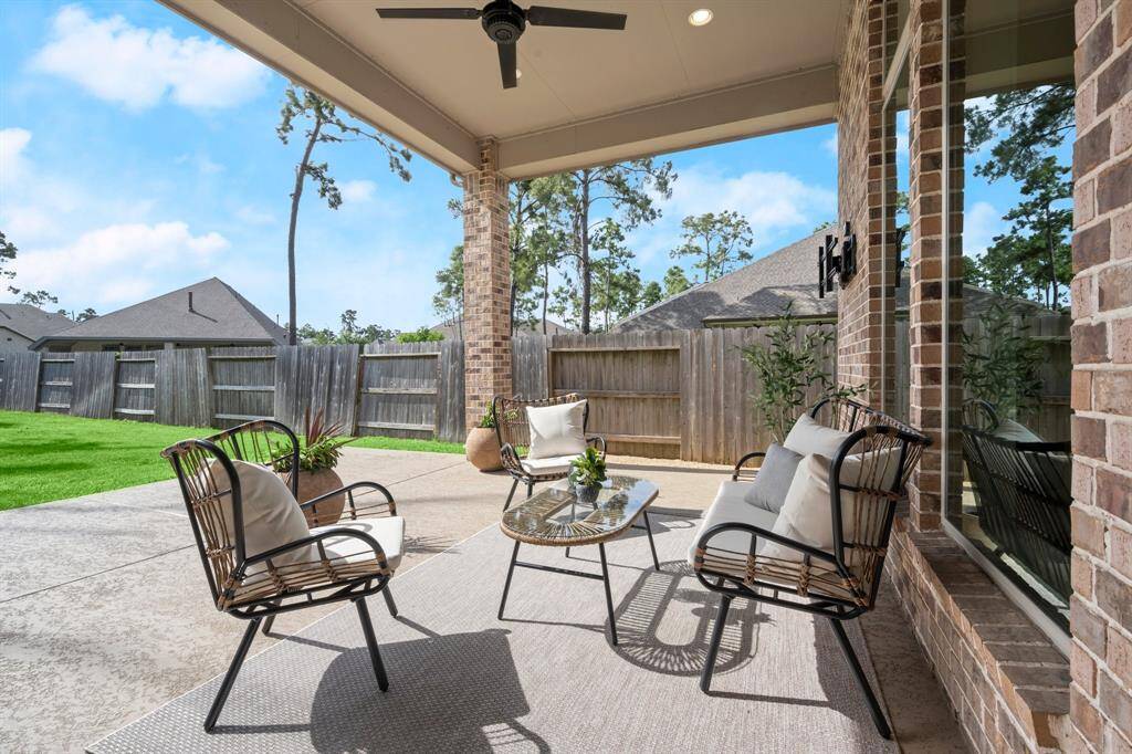 Discover a charming covered patio with stylish seating and a ceiling fan, overlooking a lush, fenced backyard—ideal for relaxation and entertaining.