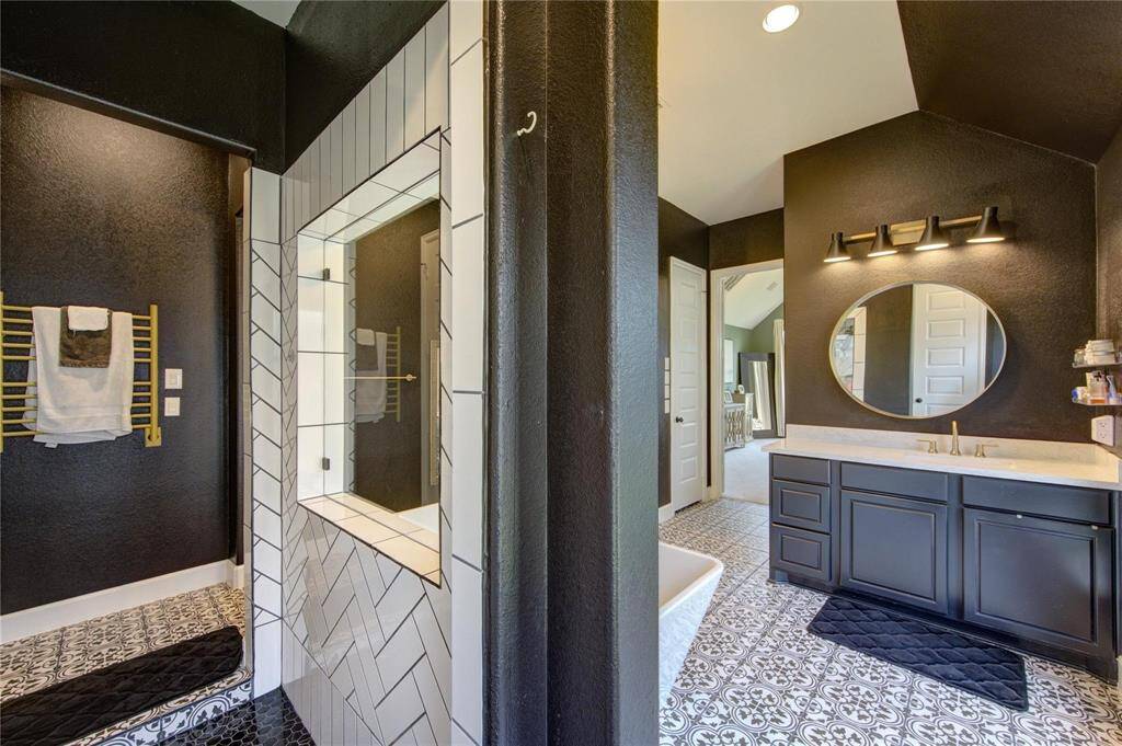 Modern primary bathroom featuring bold black walls, patterned tile flooring, and a sleek double vanity with round mirrors. The shower has a stylish herringbone tile design in this well-lit contemporary space.