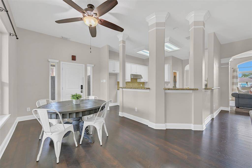 Charming breakfast nook with warm Pergo wood floors and natural light, seamlessly connected to the kitchen by columned openings and a raised granite bar—ideal for casual dining or morning coffee with a view of the backyard oasis!