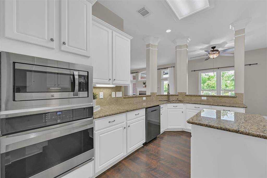 Sleek stainless steel built-in microwave and oven combo complement the granite counters and white cabinetry. Under-cabinet lighting and a raised breakfast bar enhance both style and function in this well-designed culinary space.