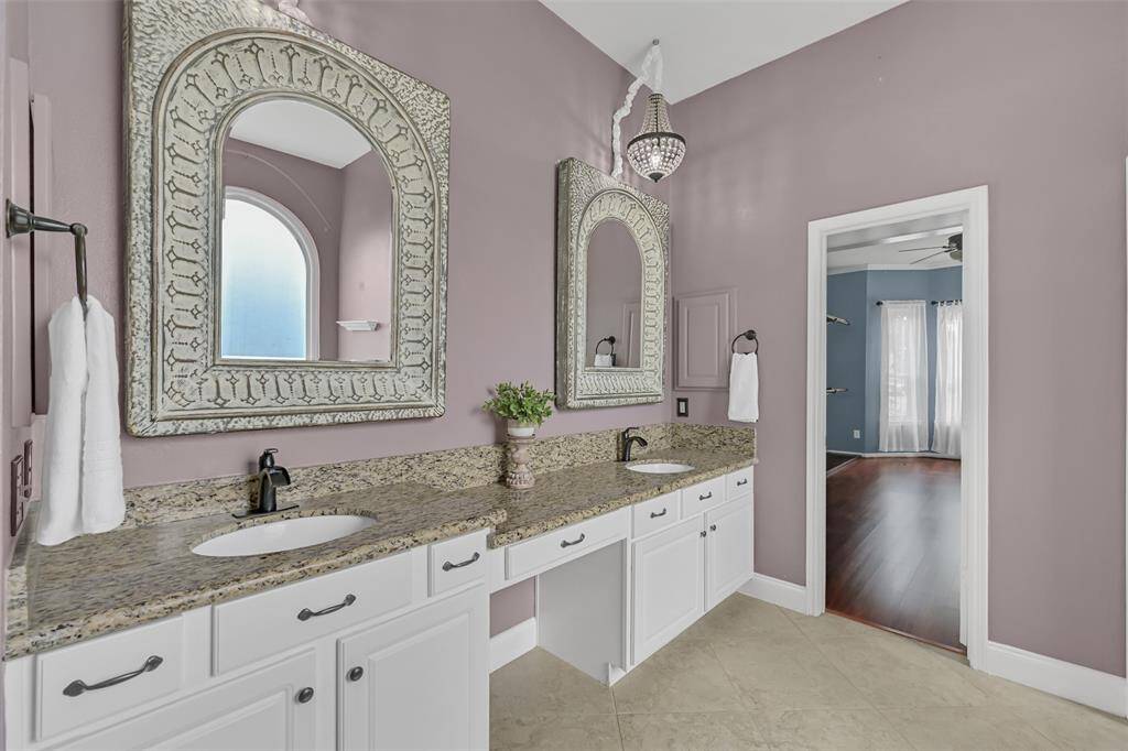 Updated in 2022, this stylish en suite master bathroom offers dual granite-topped vanities with undermount sinks with waterfall faucets, decorative framed mirrors, elegant lighting, and a built-in seated makeup vanity.