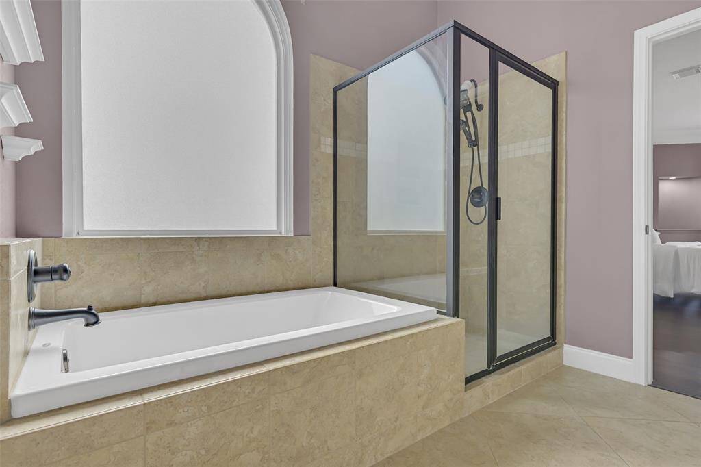Unwind in the spa-like en-suite with a deep soaking tub, walk-in shower with seating, oil-rubbed bronze fixtures, and tile surround—all beneath a frosted arched window that offers both light and privacy.