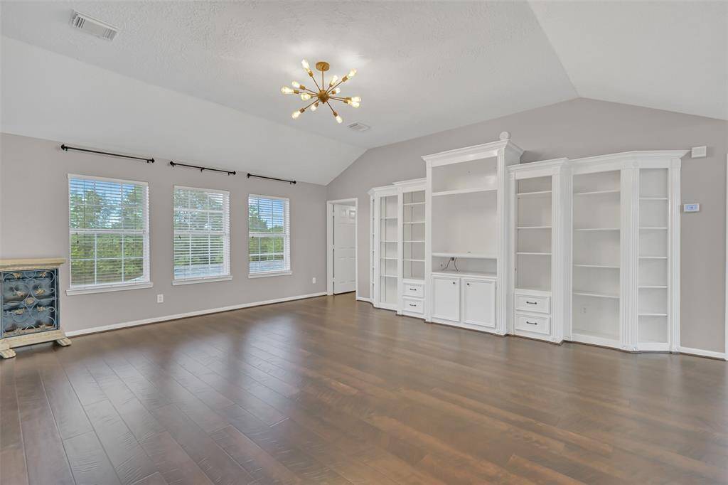 Alternate view of the spacious upstairs game room, featuring built-in shelving for display or media storage, abundant natural light from triple windows, and durable Pergo 24+ flooring—an inviting space for fun, study, or relaxation.