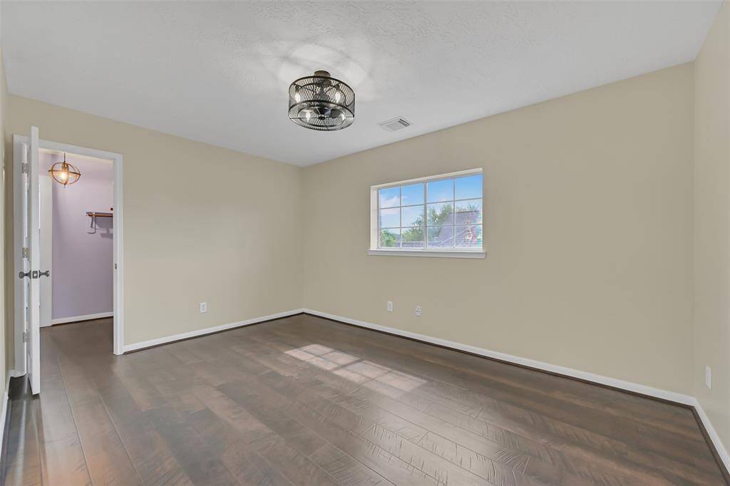 The first of three spacious upstairs secondary bedrooms features rich wood-look Pergo 24+ flooring, an upgraded modern light fixture, a side-facing window, neutral paint, and a spacious walk-in closet.