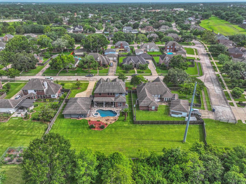 Southern aerial view showcases the resort-style pool & spa with extensive decking, the expansive L-shaped yard, covered patio with outdoor kitchen, bonus pergola retreat with swing, and a private cabana with a pool bath off of the garage—perfect for entertaining or relaxing in your own backyard oasis.