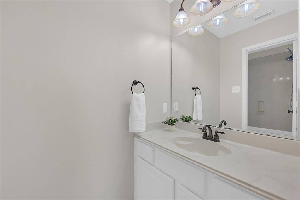 This Jack & Jill style bathroom features separate vanities for added privacy, timeless brushed bronze fixtures, white cabinetry, and a tub/shower combo with a cultured marble surround.