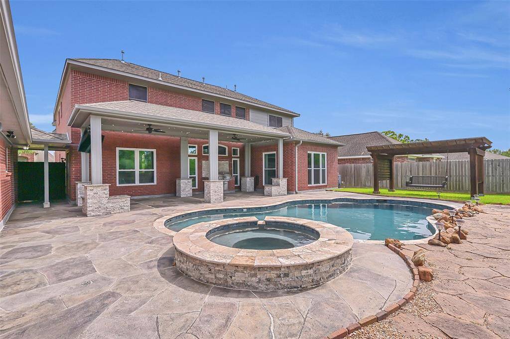 A stunning view of the full backyard retreat—featuring a resort-style pool and spa, an expansive Carvestone patio, a 31x13 covered outdoor living area with a built-in grill, and a charming pergola swing for peaceful relaxation.
