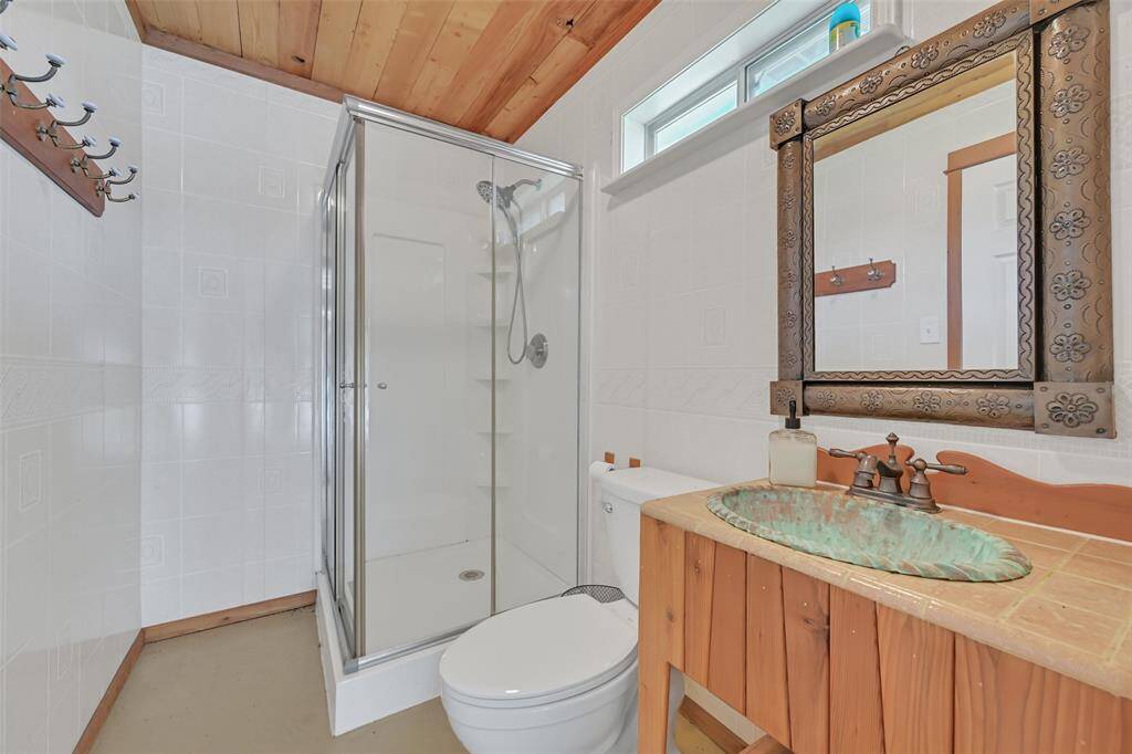 This pool bath features access from both the cabana and the expansive 5-car garage. It includes a walk-in shower, a unique copper basin sink, and a charming wood vanity beneath a matching decorative mirror—perfect for rinsing off after a day by the pool.