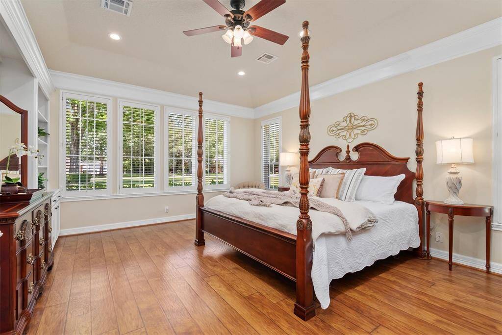 Retreat to the luxurious primary suite featuring wood floors, crown molding, a tray ceiling, and a wall of windows that fill the space with natural light—offering a peaceful and spacious haven.