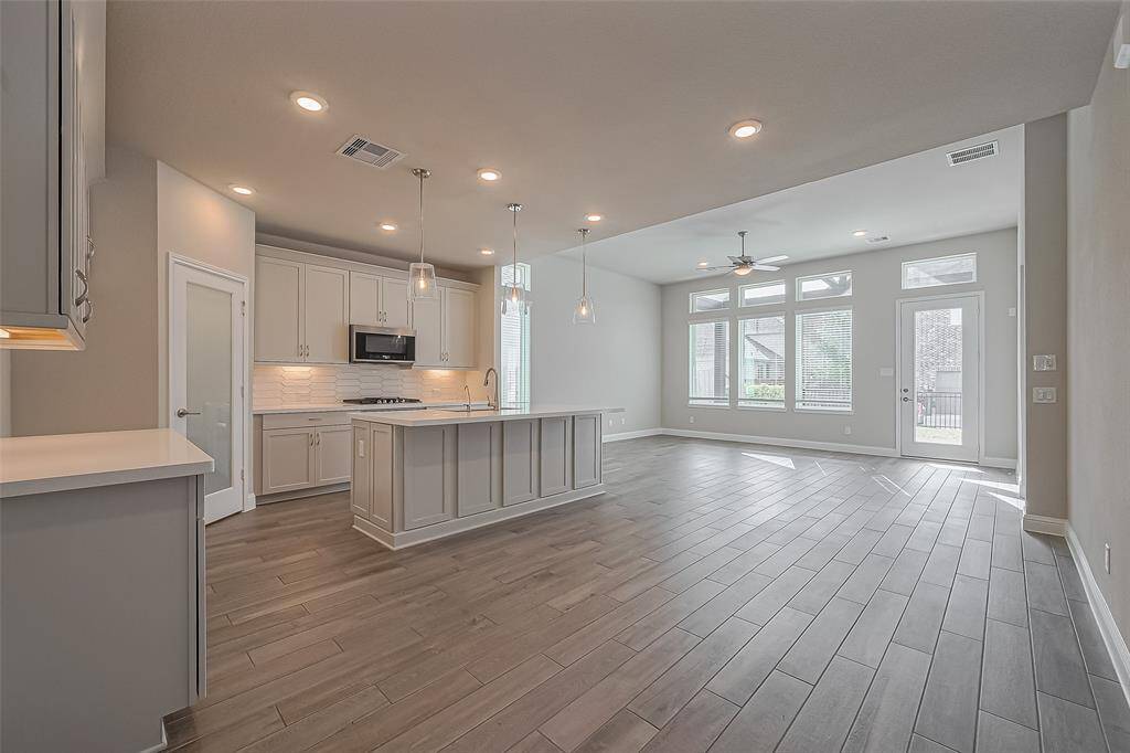 Discover this elegant open-concept living space featuring a modern kitchen with a sleek island, pendant lighting, and ample cabinetry. The expansive windows fill the room with natural light, while the stylish flooring enhances the home's contemporary charm. Perfect for entertaining and everyday living.