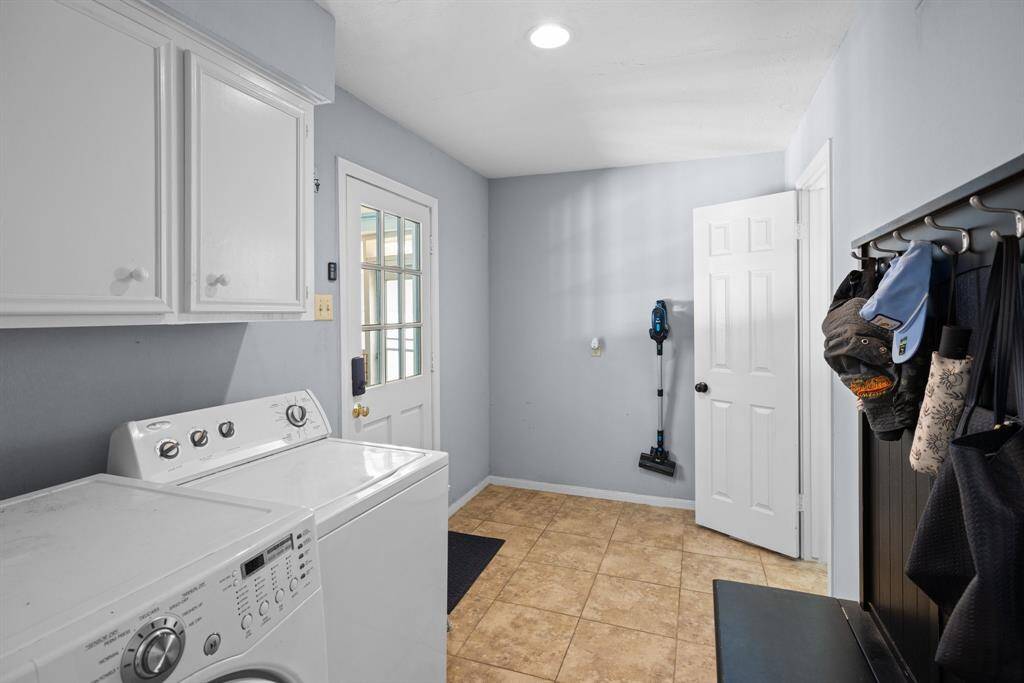 UTILITY ROOM - Large utility room has cabinets above washer & dryer.  Washer & dryer to remain.  Powder room is on the right.  The door on the left leads to the screened porch and to the garage.