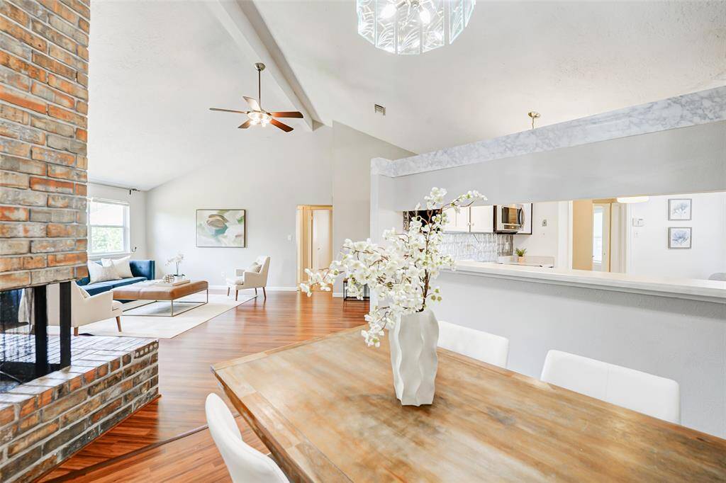This spacious, open-concept living area features high ceilings, a cozy brick fireplace, and abundant natural light. The kitchen overlooks the dining space, creating a seamless flow perfect for entertaining. Warm laminate floors add a touch of elegance throughout.