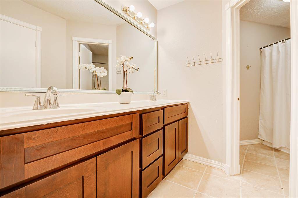 This bathroom features a spacious double vanity with rich wood cabinets, modern fixtures, and a large mirror. The shower/tub combo and toilet are in a separate area giving each person privacy.