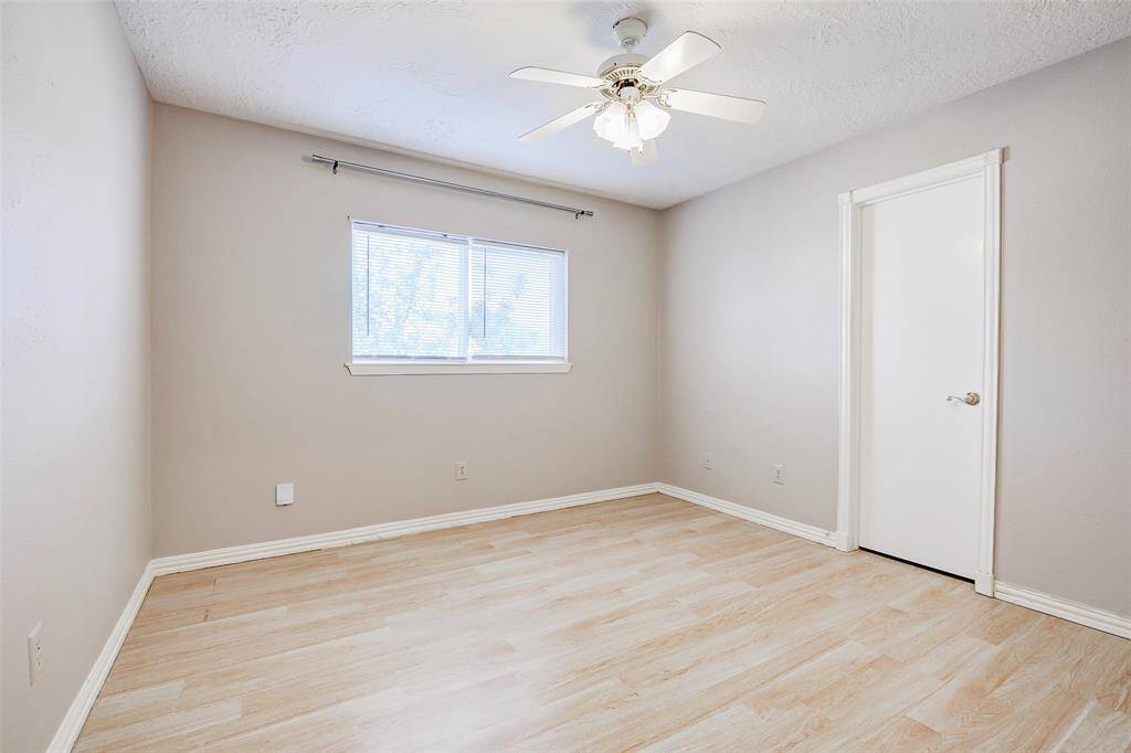 This bedroom features light laminate flooring, neutral walls, a ceiling fan, and a window for natural light.