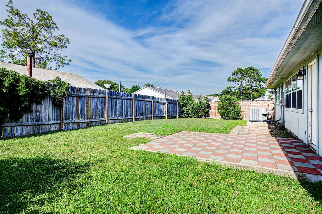 This photo shows a spacious backyard featuring a green lawn, a tiled patio area, and a wooden fence for privacy. It's ideal for outdoor activities and entertaining.